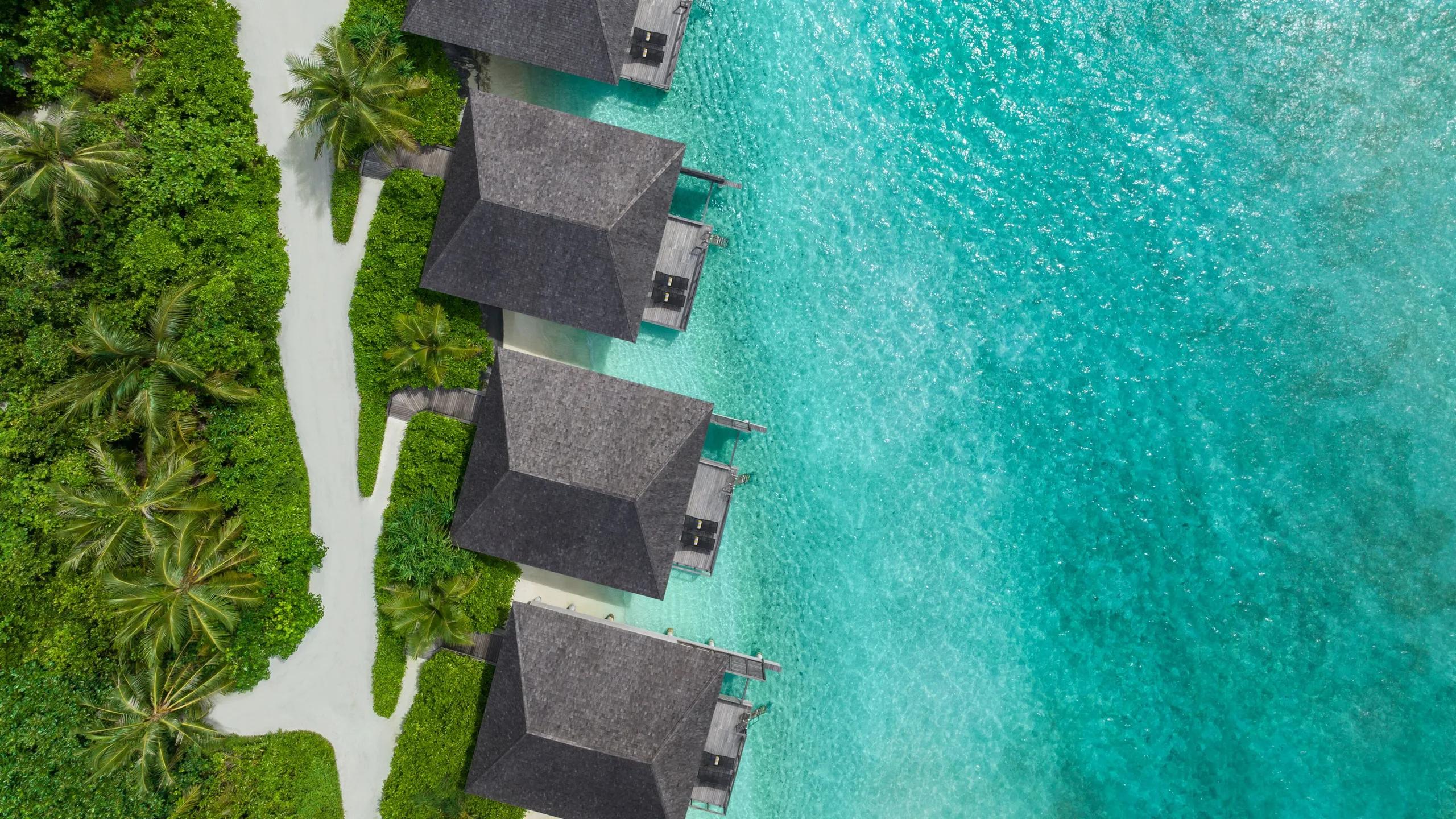 Overwater villa roofs set directly above the turquoise lagoon at Le Méridien Maldives, seen from above