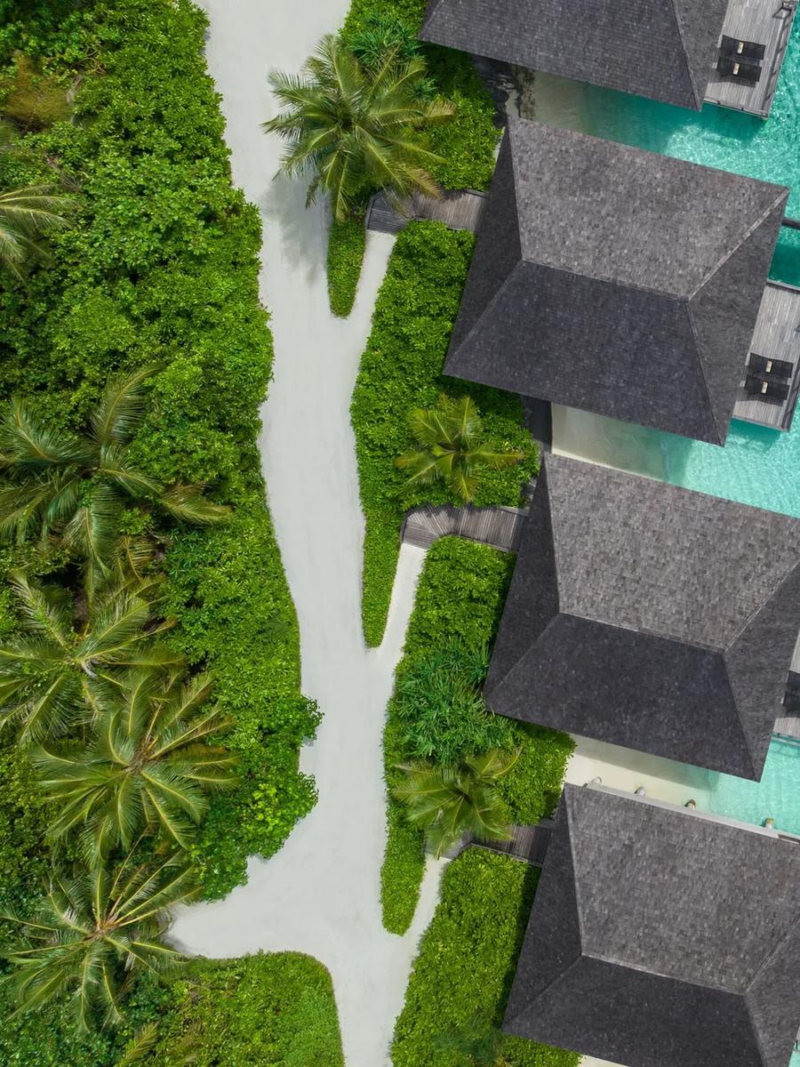 Overwater villa roofs set directly above the turquoise lagoon at Le Méridien Maldives, seen from above