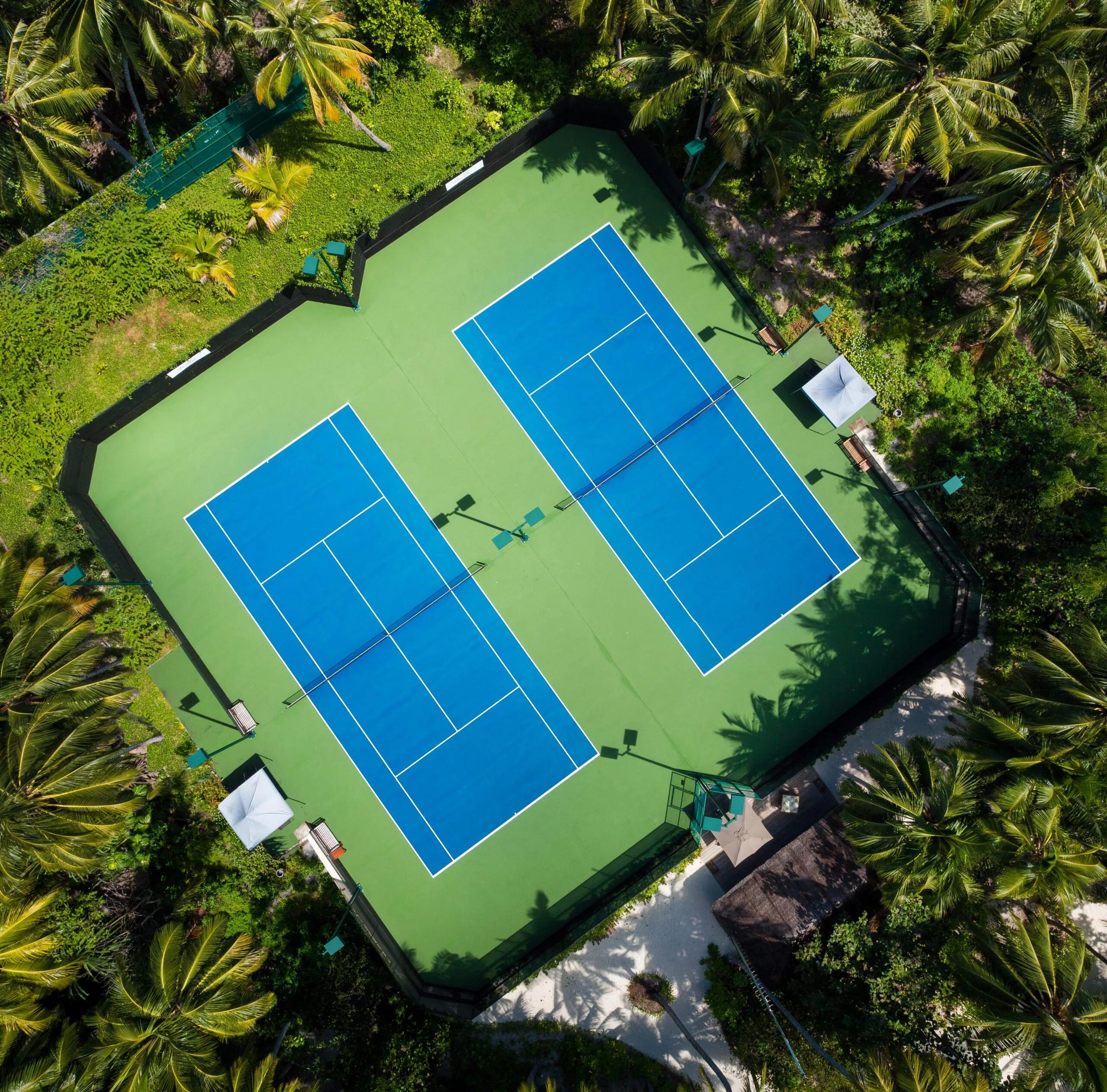 Amilla's tennis courts seen directly from above, two blue courts set in a clearing among the palms
