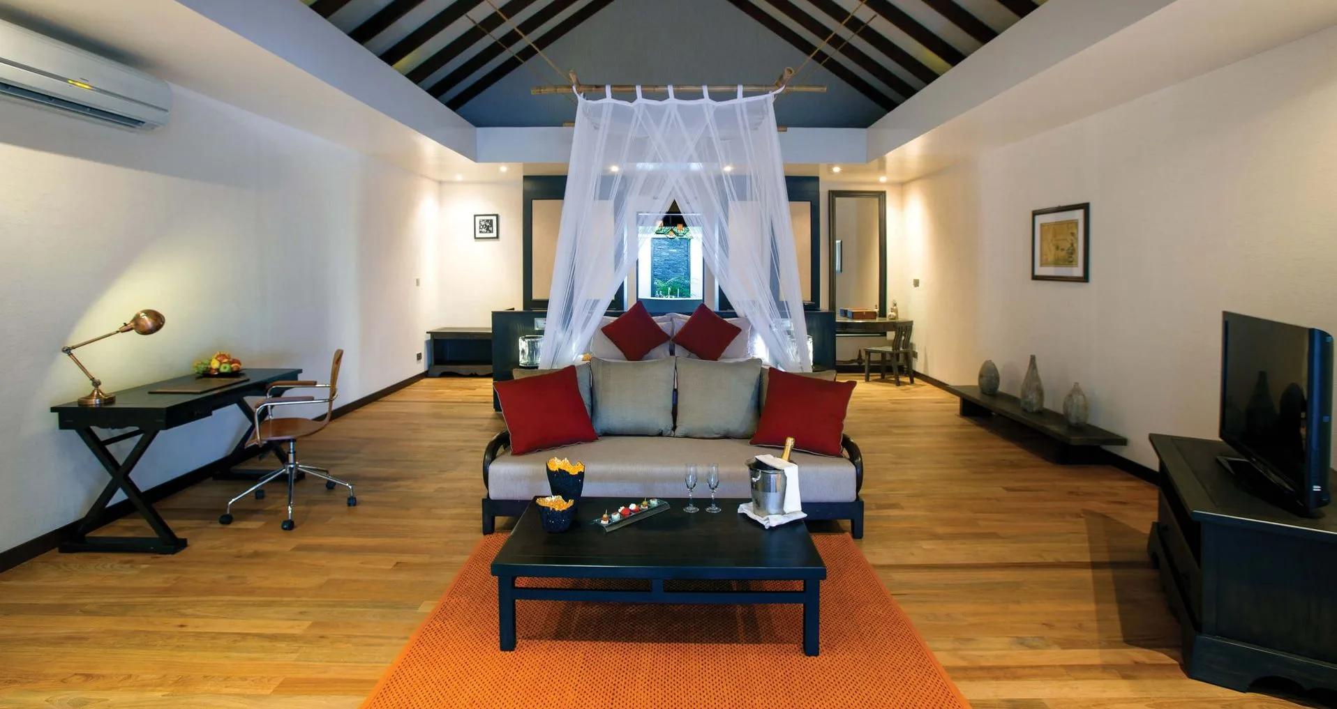The living area of a Sunset Beach Villa, its four-poster netting canopy over the bed and a sofa beyond