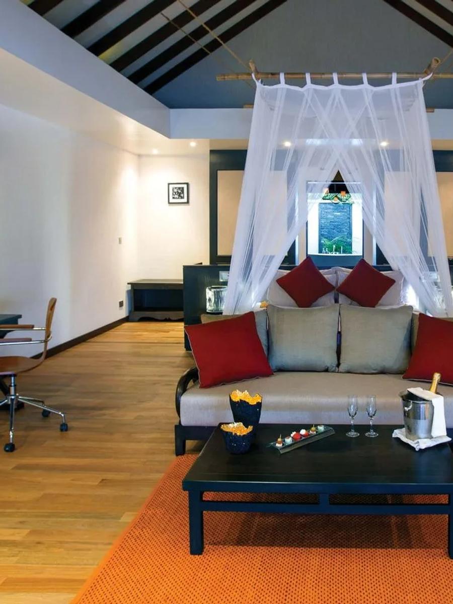 The living area of a Sunset Beach Villa, its four-poster netting canopy over the bed and a sofa beyond