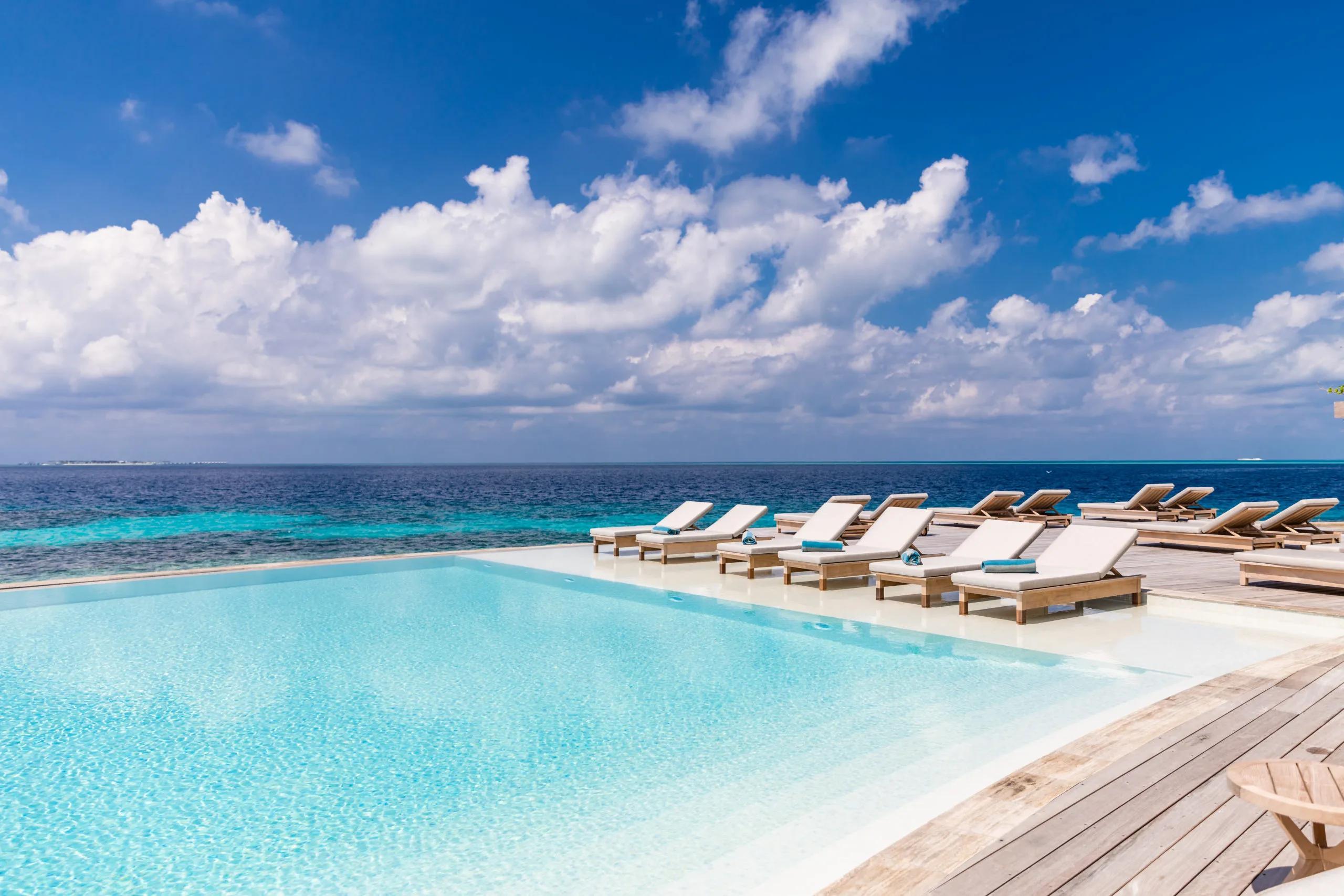 An infinity pool's edge merging into the open ocean, a row of cushioned sun loungers along the deck