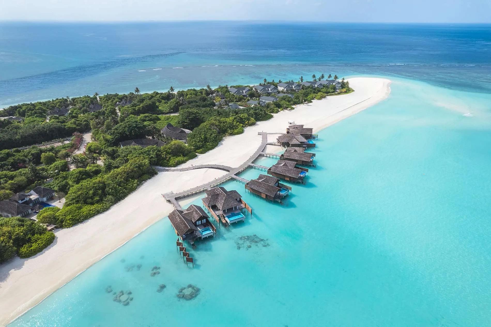 Aerial view of Hideaway's overwater villa row reaching out from the beach into the lagoon