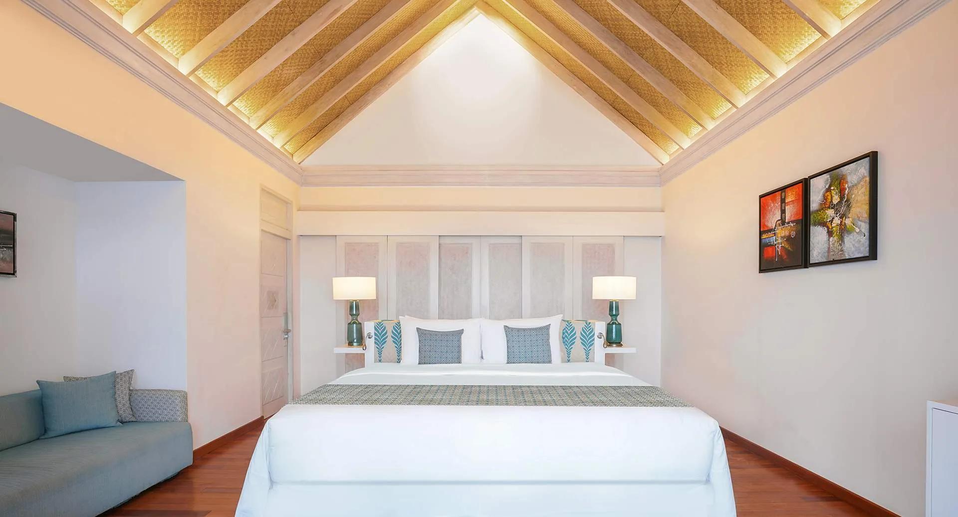 The bedroom of an Over Water Villa with Private Pool, beneath a pitched thatched ceiling