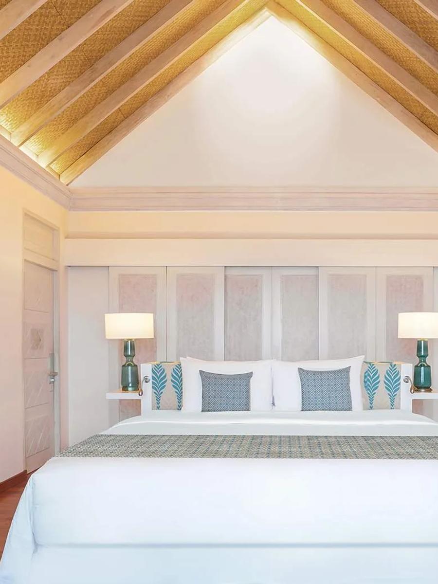 The bedroom of an Over Water Villa with Private Pool, beneath a pitched thatched ceiling