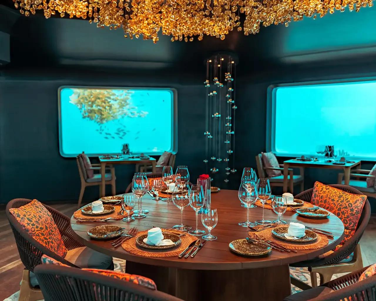 Bubble's underwater dining room, a table set beneath a gold chandelier with reef fish visible through the windows