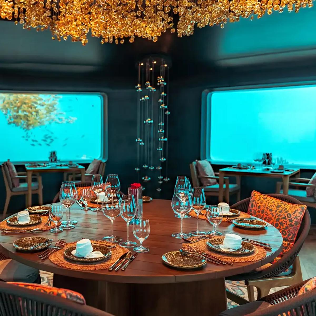Bubble's underwater dining room, a table set beneath a gold chandelier with reef fish visible through the windows