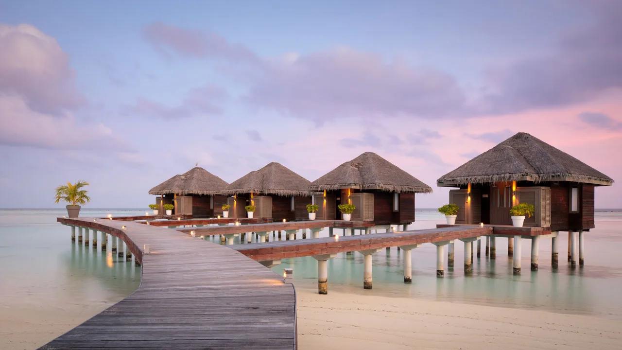 The boardwalk to LUX* Me Spa's overwater treatment villas at dusk, lanterns lit along the railing