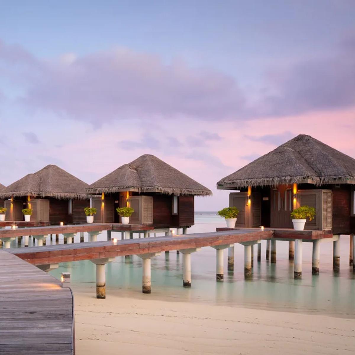 The boardwalk to LUX* Me Spa's overwater treatment villas at dusk, lanterns lit along the railing