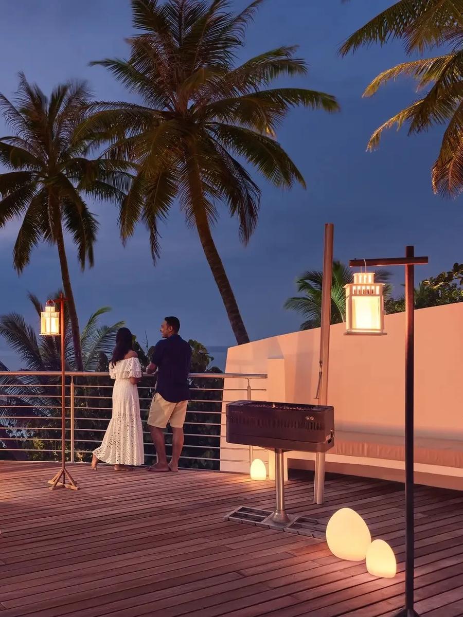A private dinner set on a villa's roof terrace at dusk, lanterns lit and the overwater villa row visible across the water