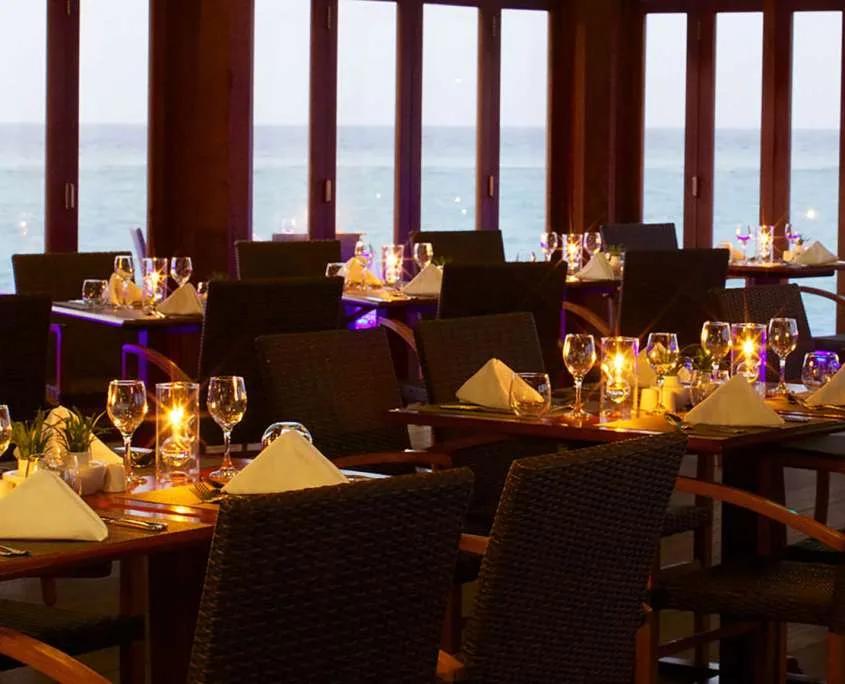 O Restaurant's candlelit tables facing floor-to-ceiling windows onto the ocean at dusk