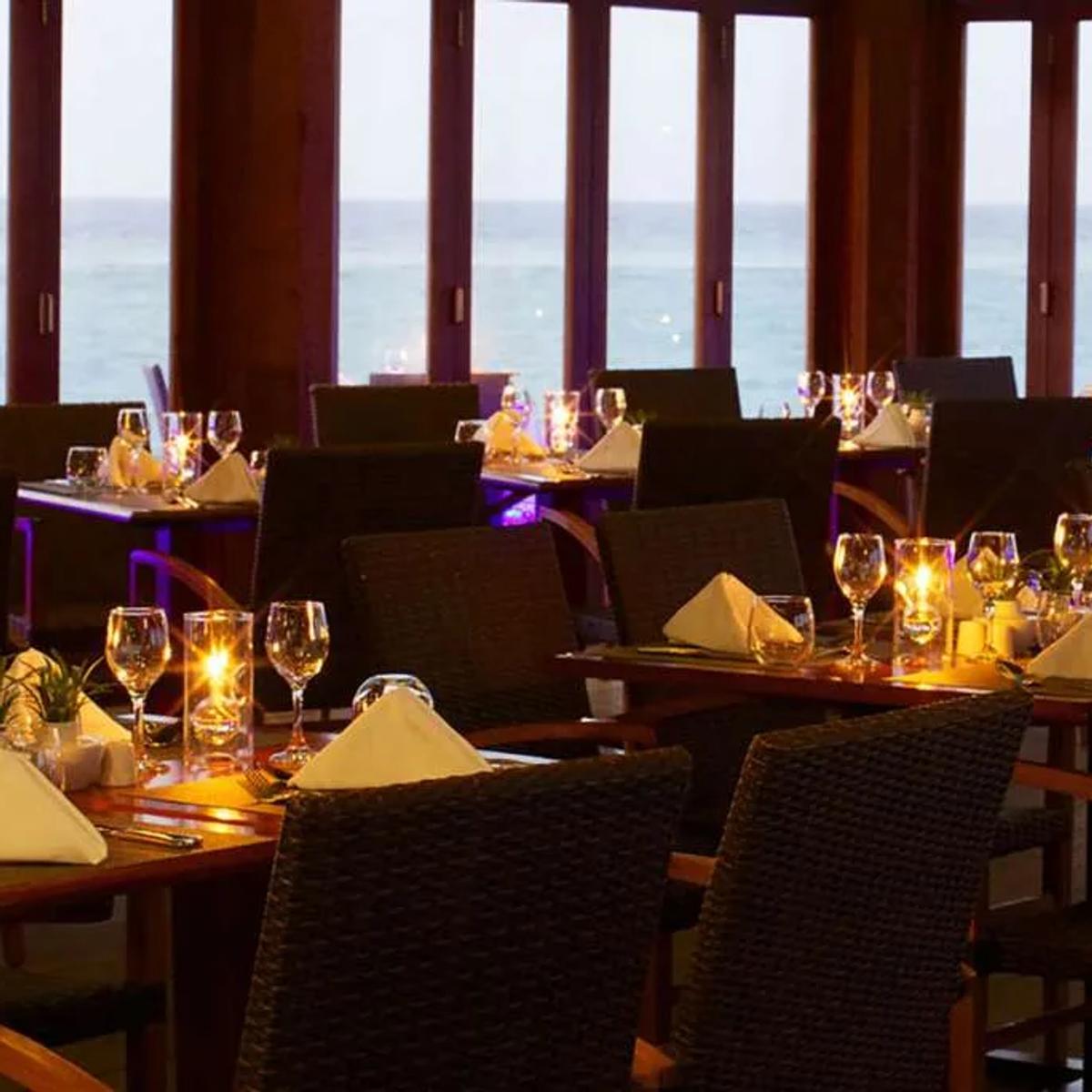 O Restaurant's candlelit tables facing floor-to-ceiling windows onto the ocean at dusk