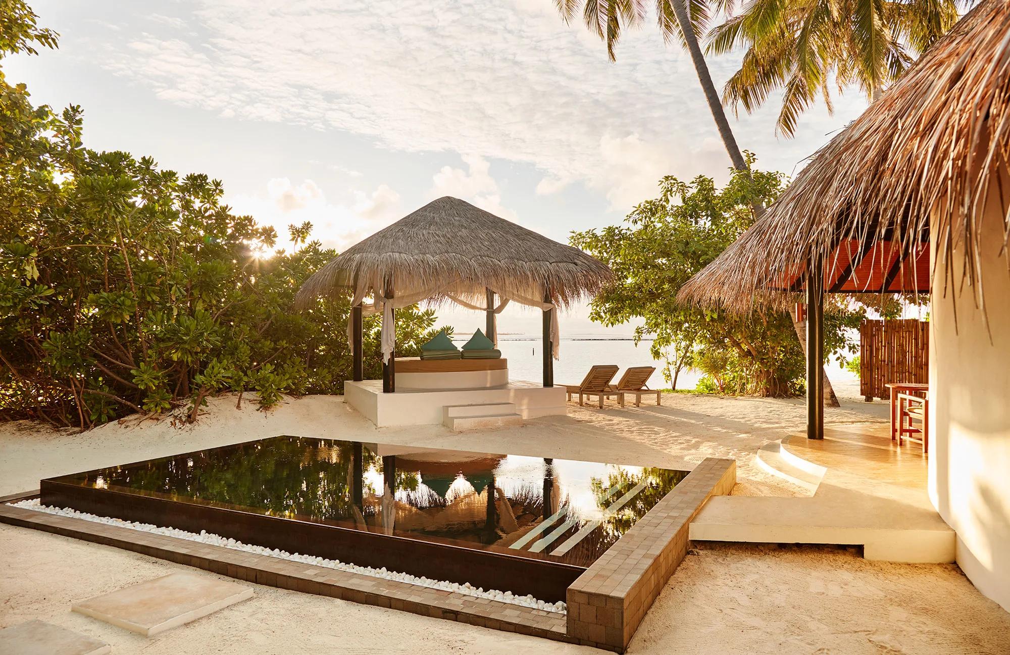 A private plunge pool and thatched beach sala lit by sunset, steps from the sand at a Family Deluxe Beach Villa with Pool