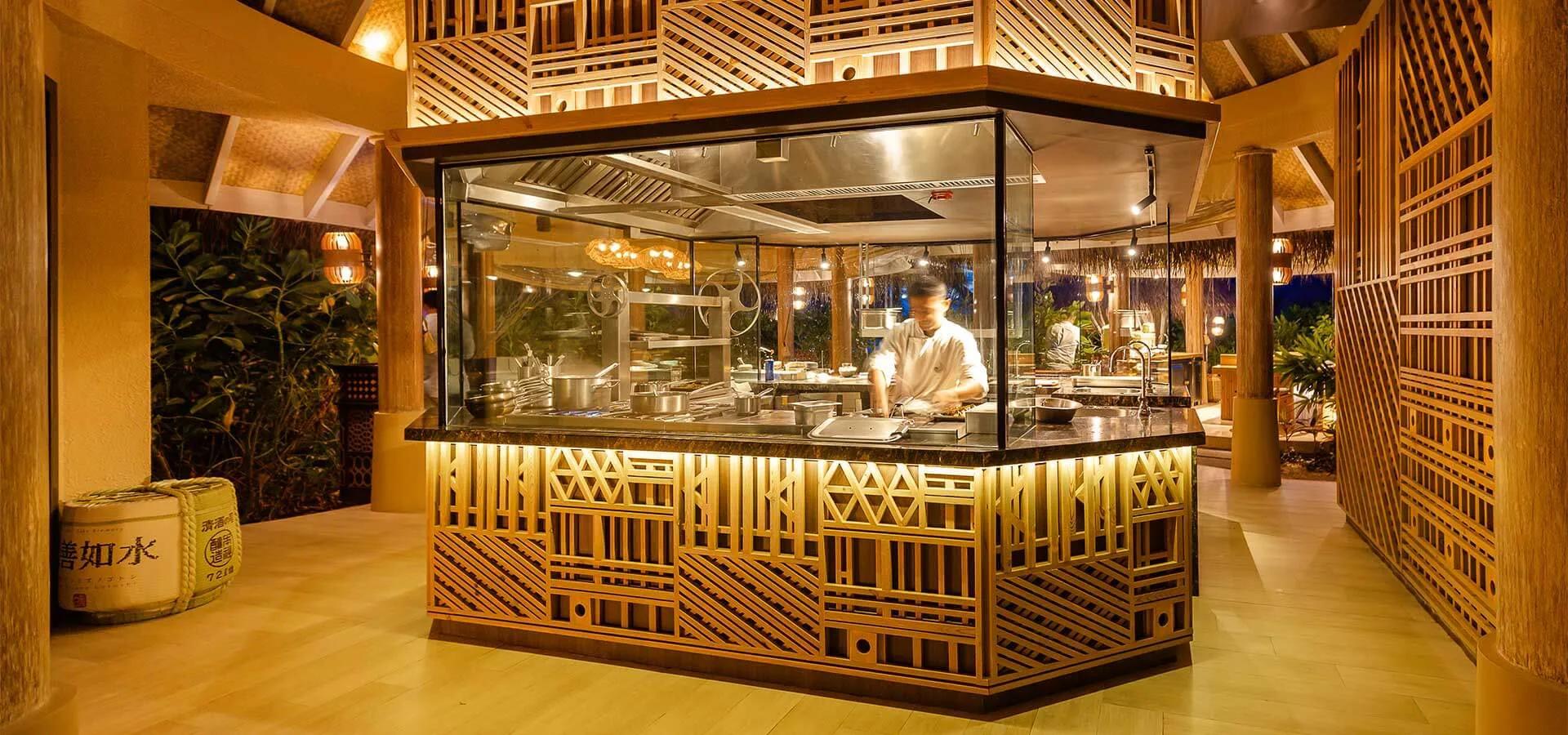 A chef working the open kitchen at Ocaso after dark, sake bottles displayed at the pass.