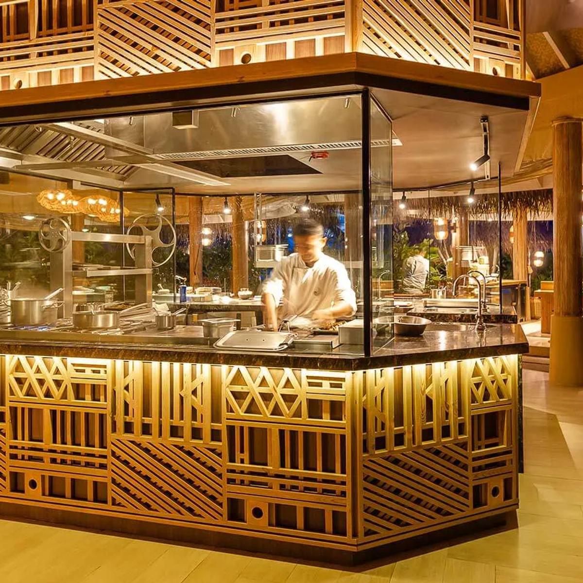 A chef working the open kitchen at Ocaso after dark, sake bottles displayed at the pass.