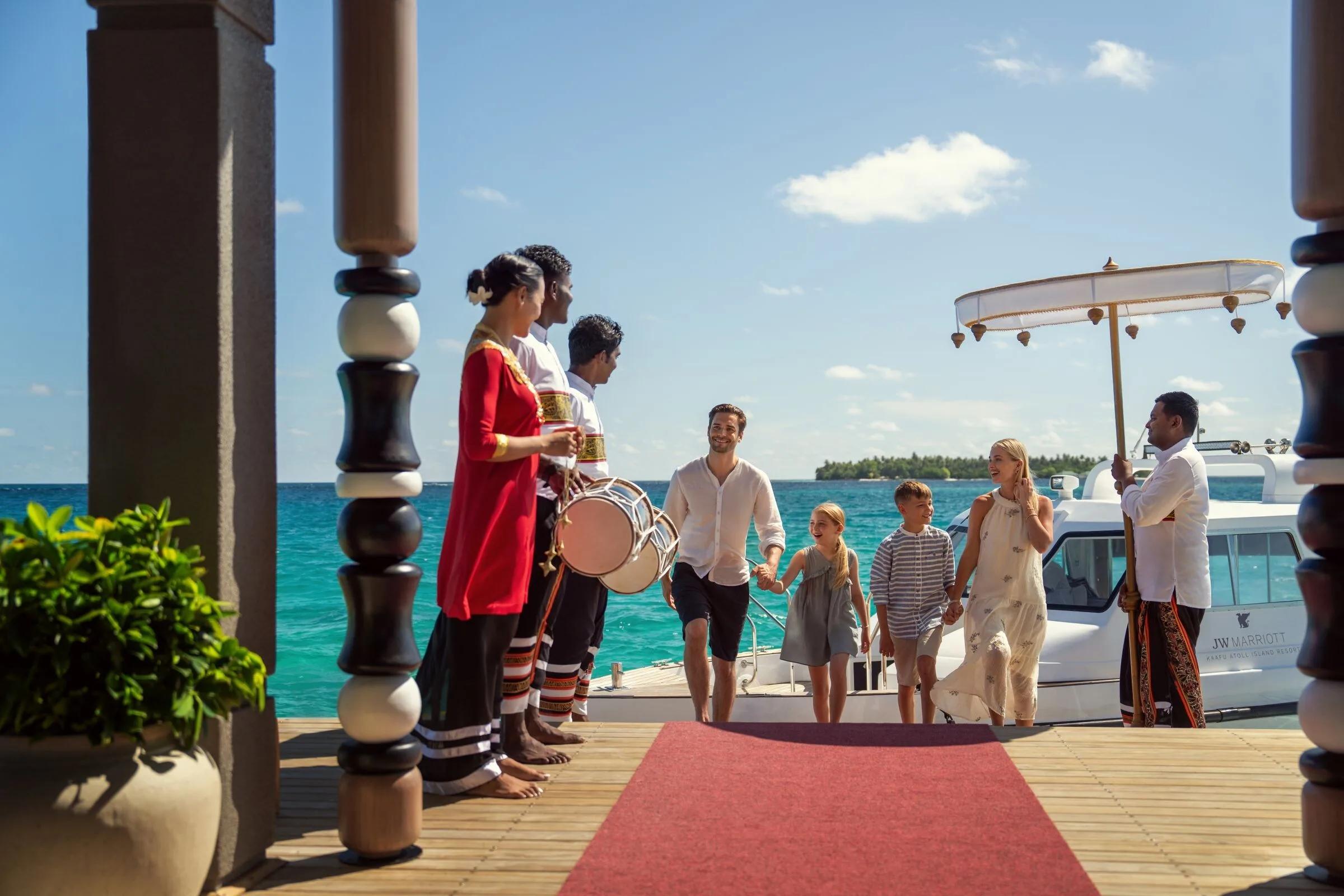 A family welcomed at JW Marriott Maldives Kaafu Atoll's arrival jetty with a traditional drum ceremony and red-carpet greeting