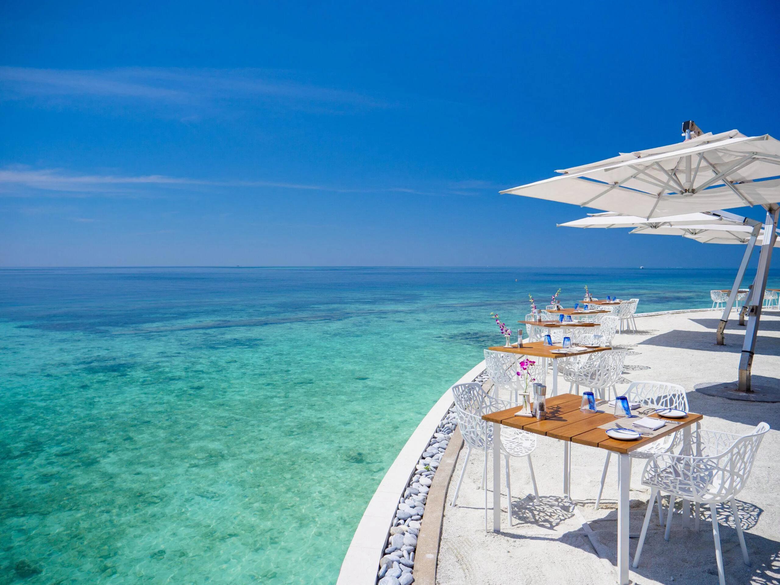 Celsius's oceanfront terrace, tables set under umbrellas at the reef's edge