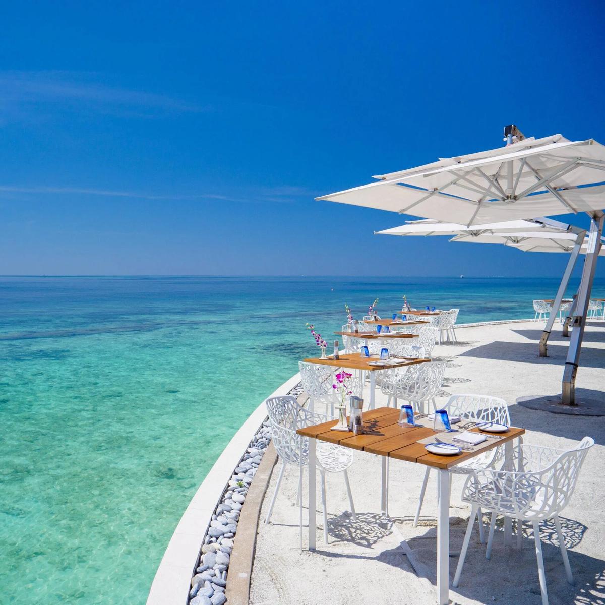 Celsius's oceanfront terrace, tables set under umbrellas at the reef's edge