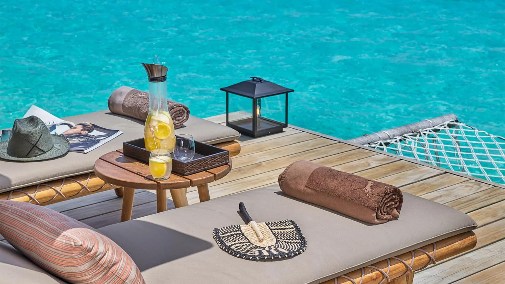 A water villa's deck with lounge chairs, a hammock net and drinks laid out over the lagoon — Two Bedroom Water Villa photograph to follow