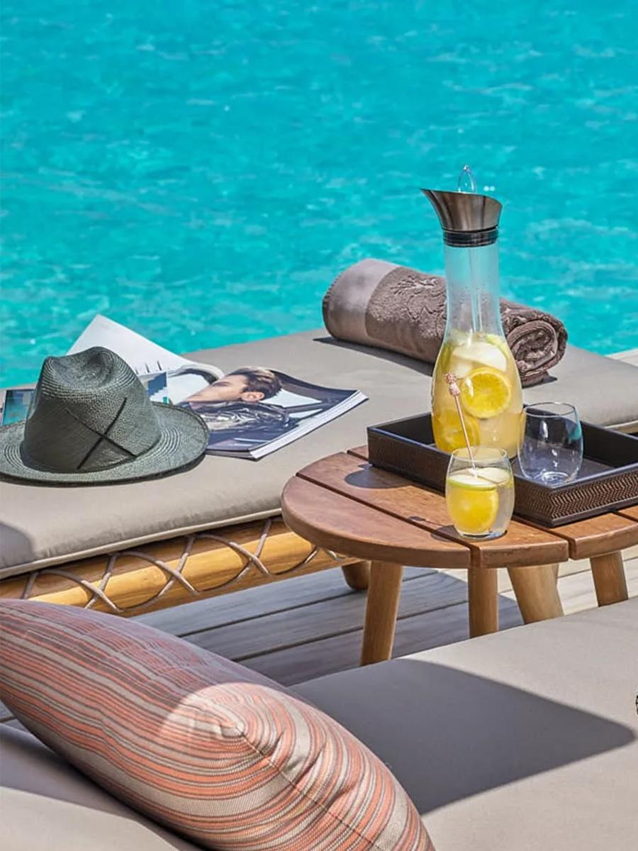 A water villa's deck with lounge chairs, a hammock net and drinks laid out over the lagoon — Two Bedroom Water Villa photograph to follow