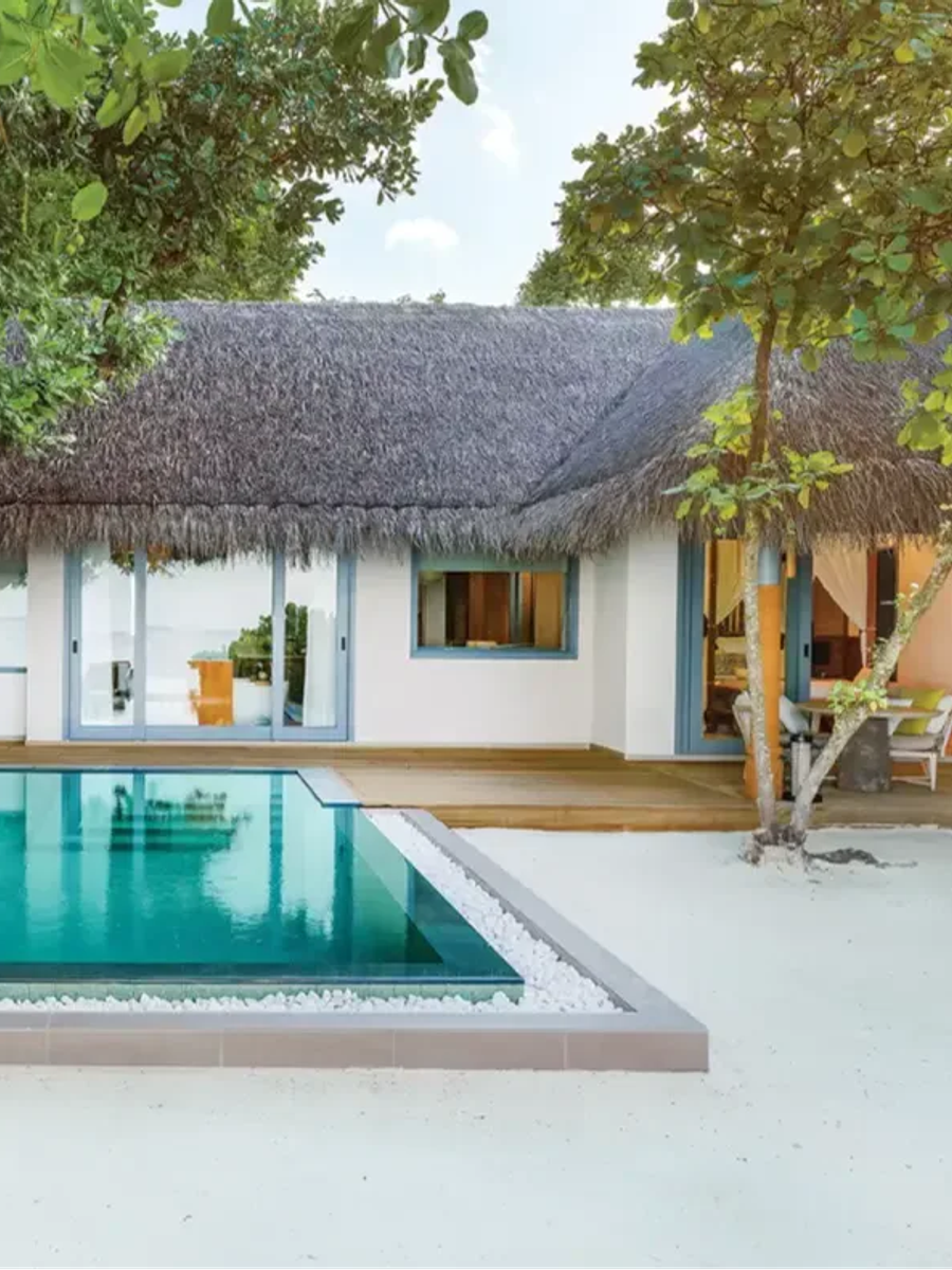 A Beach Pool Villa's rectangular pool in front of a thatched-roof villa, sun deck and lounge area visible through the open doors