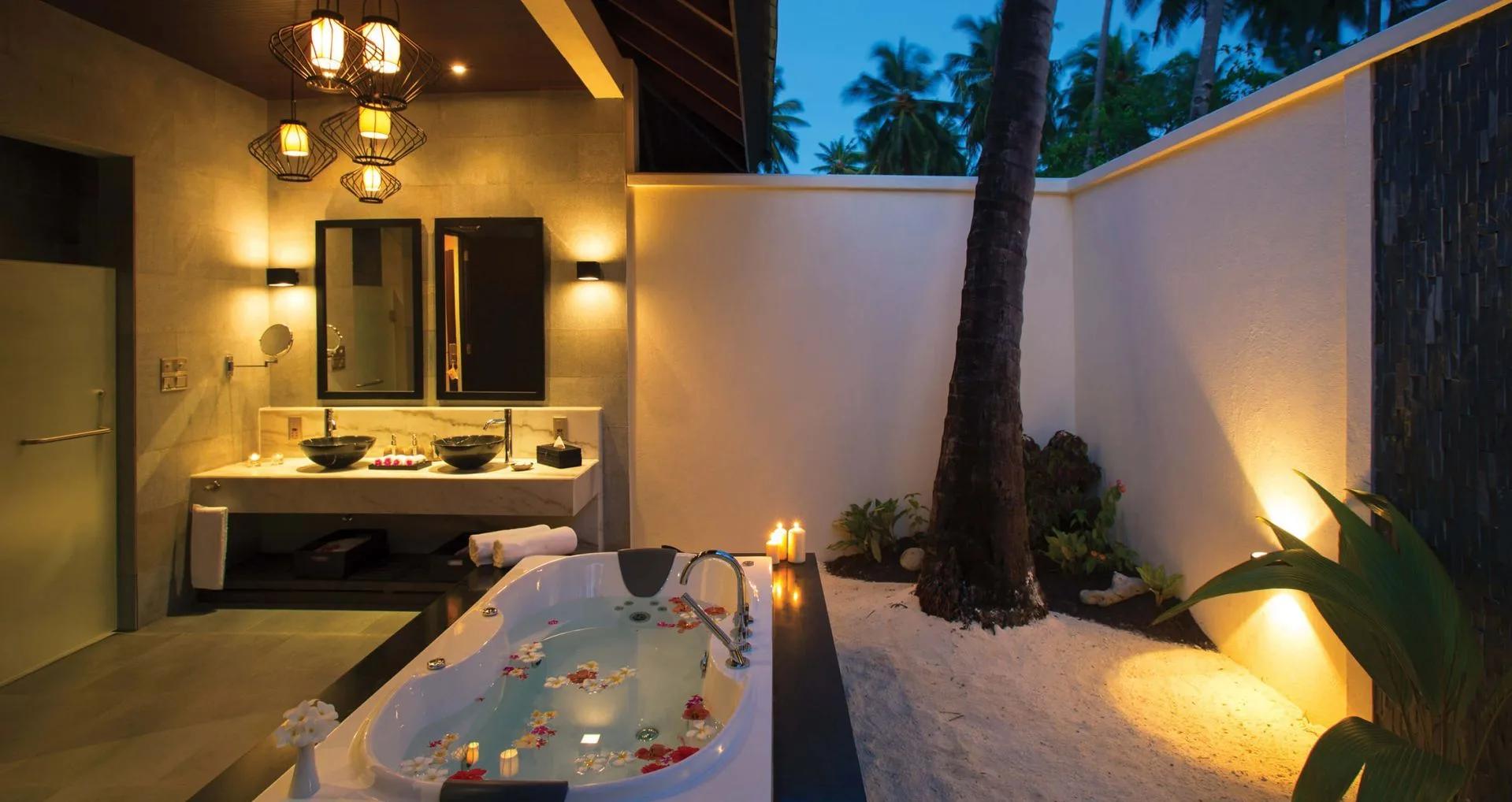A Sunset Beach Villa's outdoor bath, steps from the bedroom and lit by hanging pendant lights at dusk
