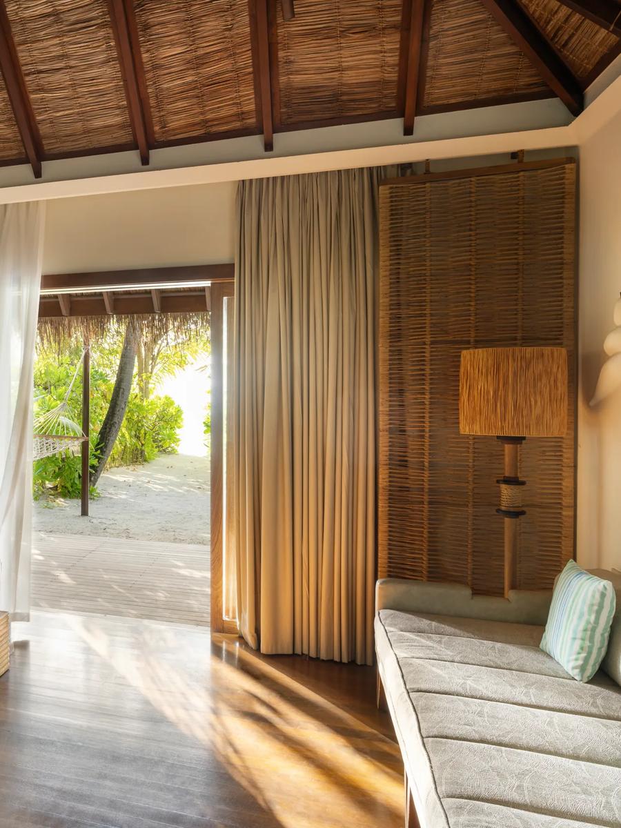 A Beach Villa bedroom with a rope-and-bamboo headboard, sheer curtains drawn back to a garden deck with a hammock and sunloungers