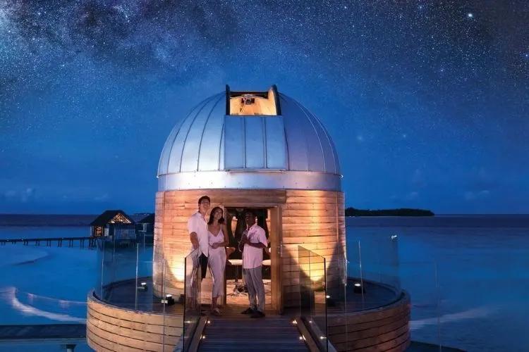 An overwater dinner table lit above a dark Maldives lagoon at night