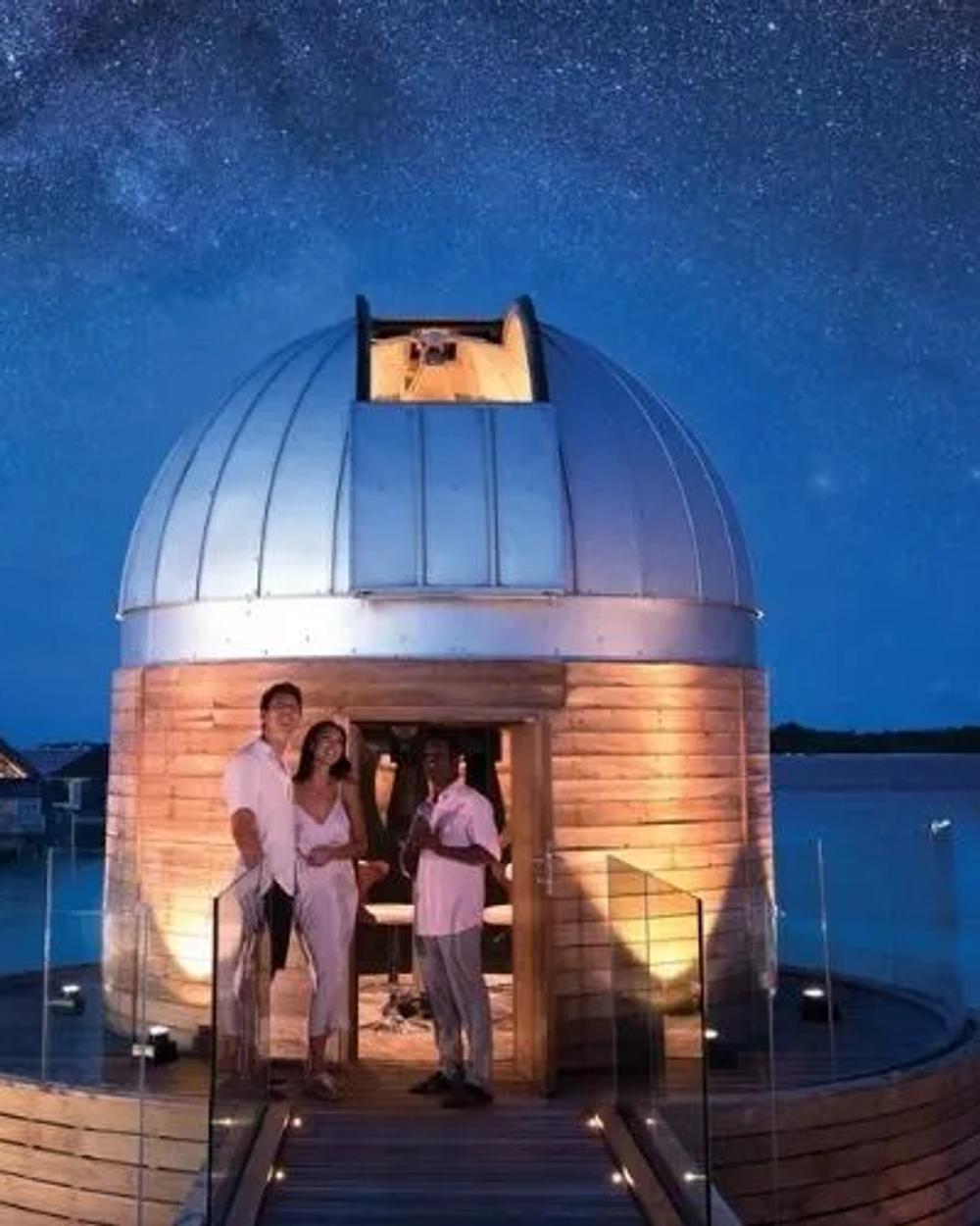 An overwater dinner table lit above a dark Maldives lagoon at night