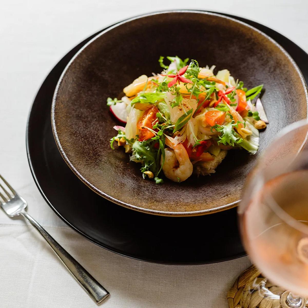 A plated shrimp and herb salad beside a glass of sparkling wine, representative of Iru Fushi's overwater bar service — dedicated Bubble Lounge photography to follow