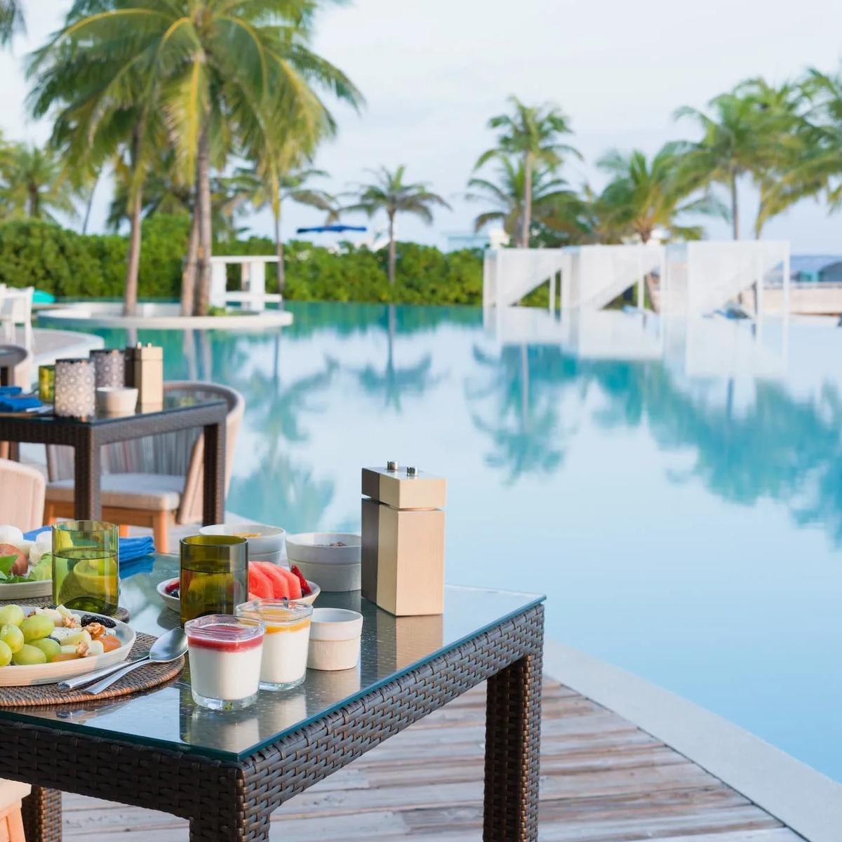 A poolside dining terrace at Amilla set for a meal; a dedicated photograph of Tessera, the resort's Arabian-inspired restaurant, was not available in this research pool