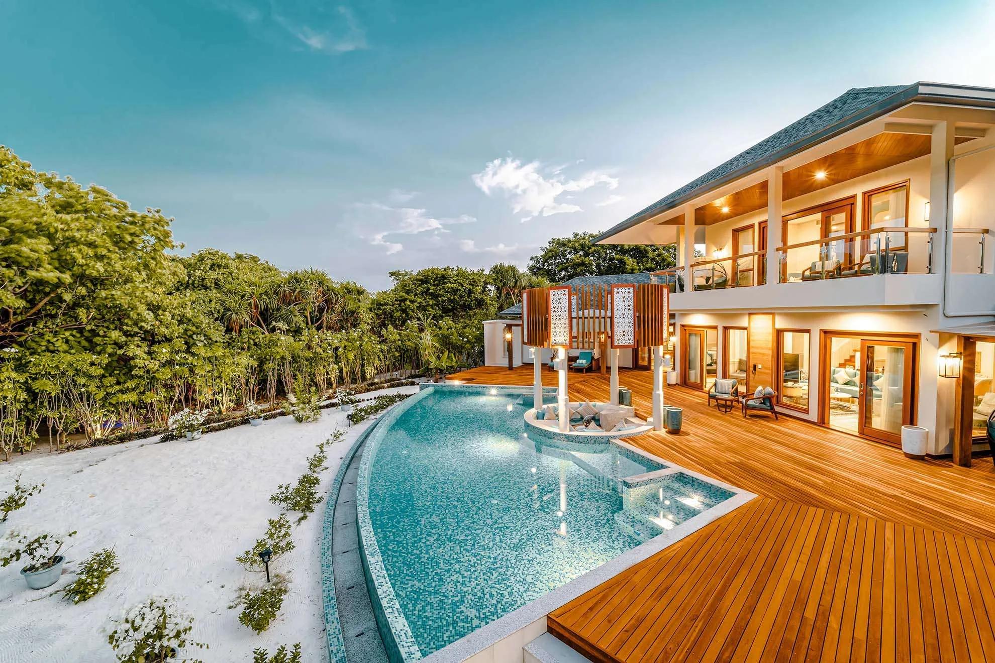 Twilight exterior of the Three-Bedroom Grand Beach Residence, its pool and two-storey villa lit warm against the dusk sky