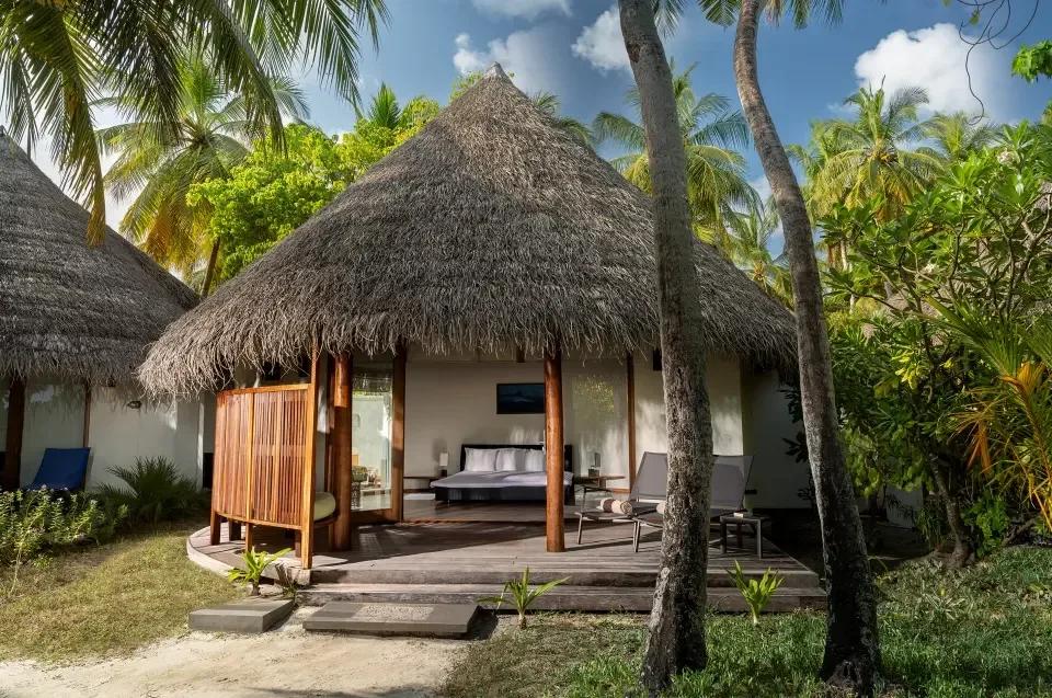 Superior Beach Villa's thatched exterior and private deck with sun loungers, set among coconut palms