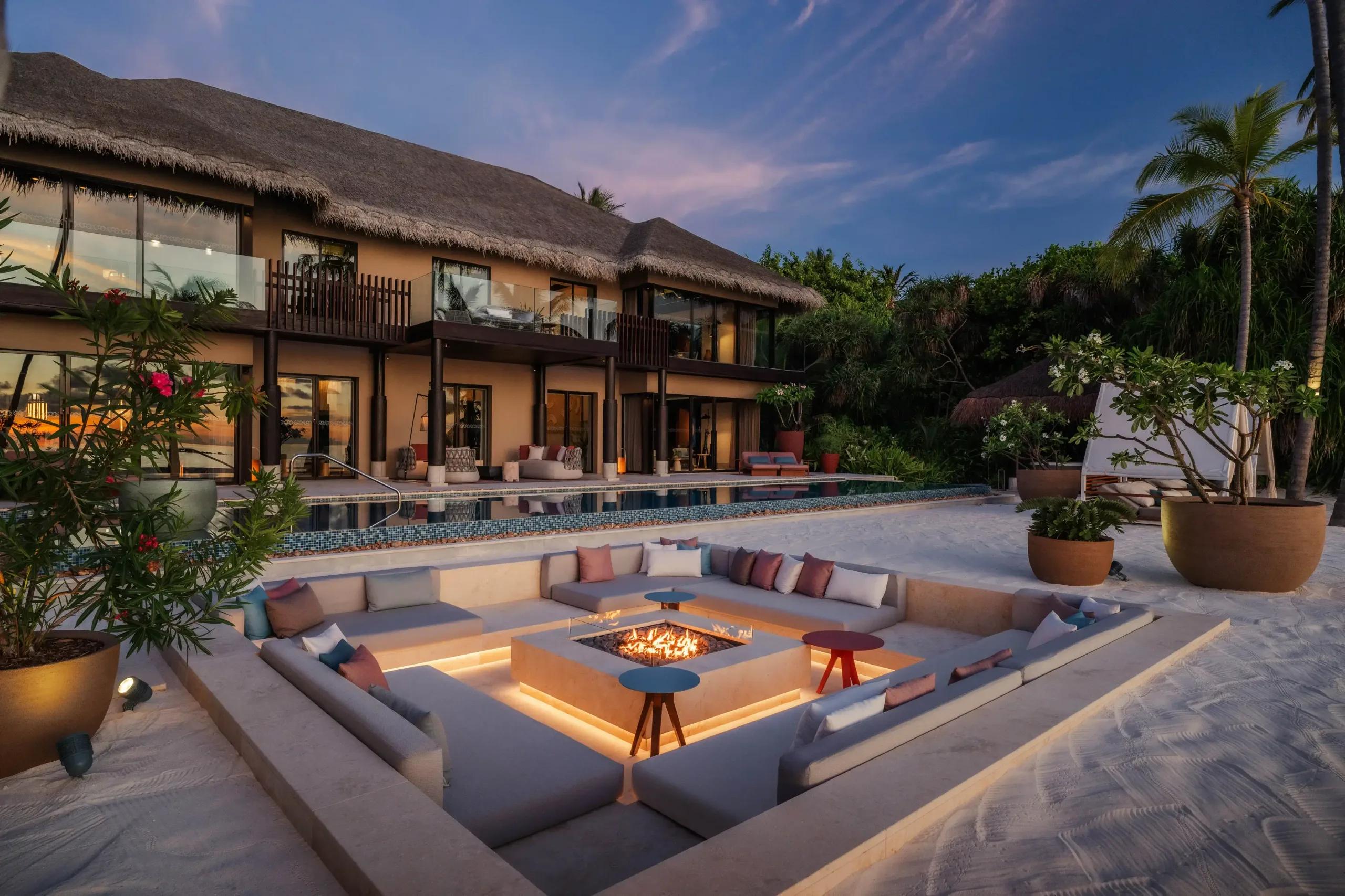 Nika Private Residence at dusk, its two-storey thatched building overlooking an infinity pool and sunken fire-pit lounge on the beach