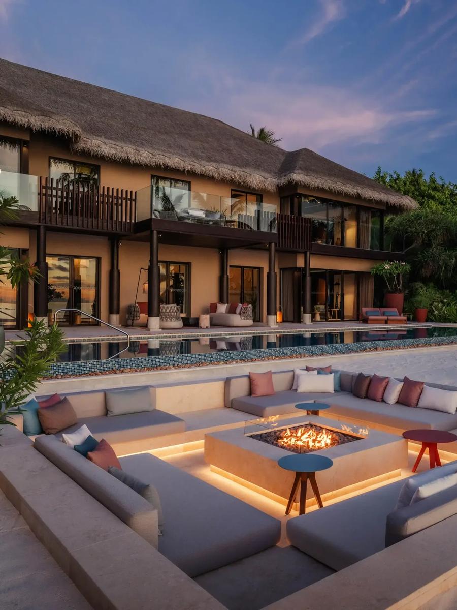 Nika Private Residence at dusk, its two-storey thatched building overlooking an infinity pool and sunken fire-pit lounge on the beach