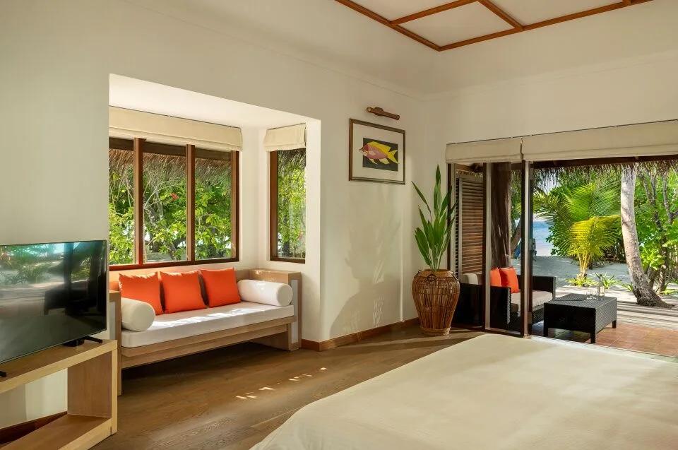 Honeymoon Pool Villa's separate living area, with a sofa dressed in orange cushions facing sliding doors open to the garden