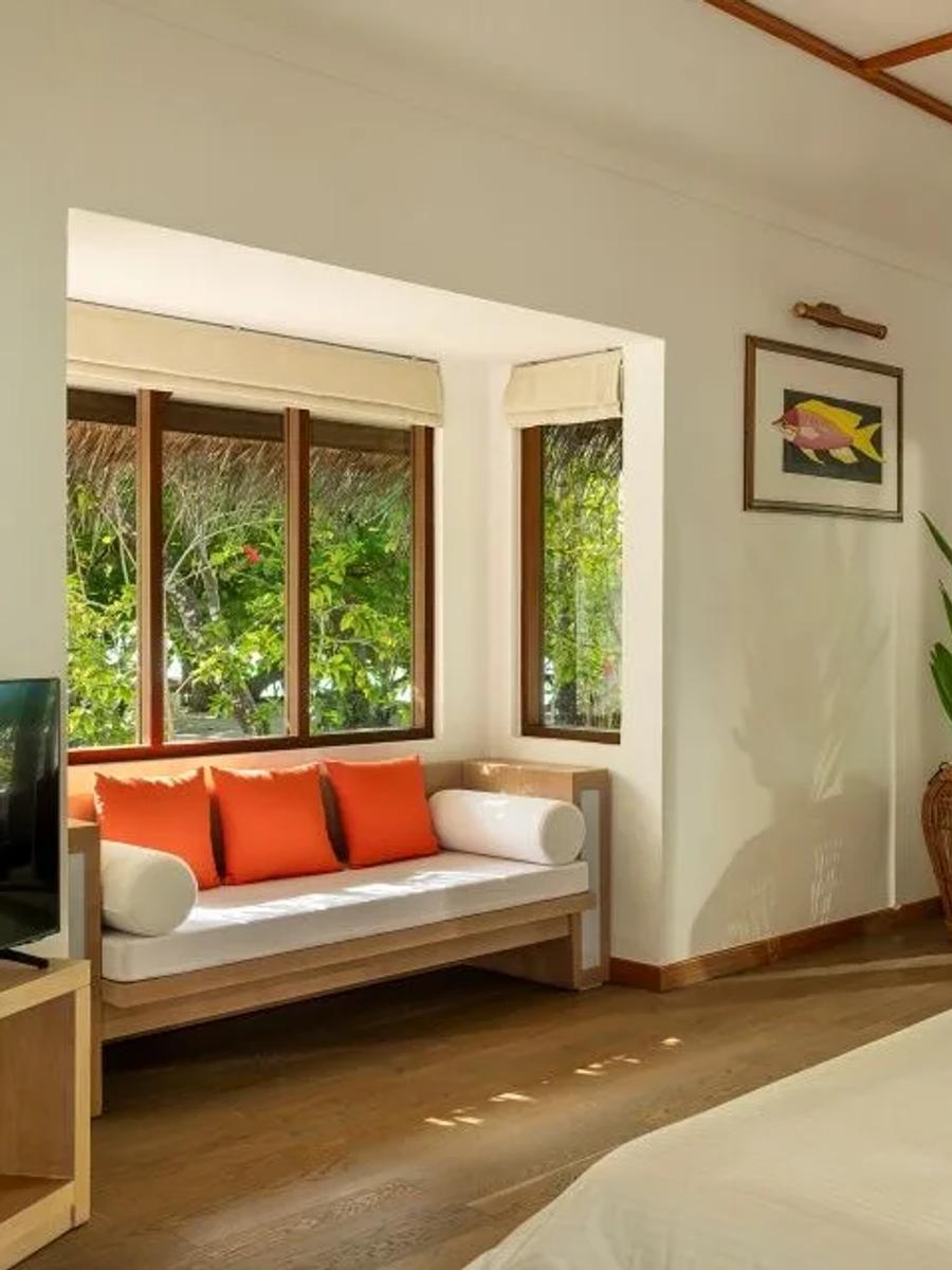 Honeymoon Pool Villa's separate living area, with a sofa dressed in orange cushions facing sliding doors open to the garden