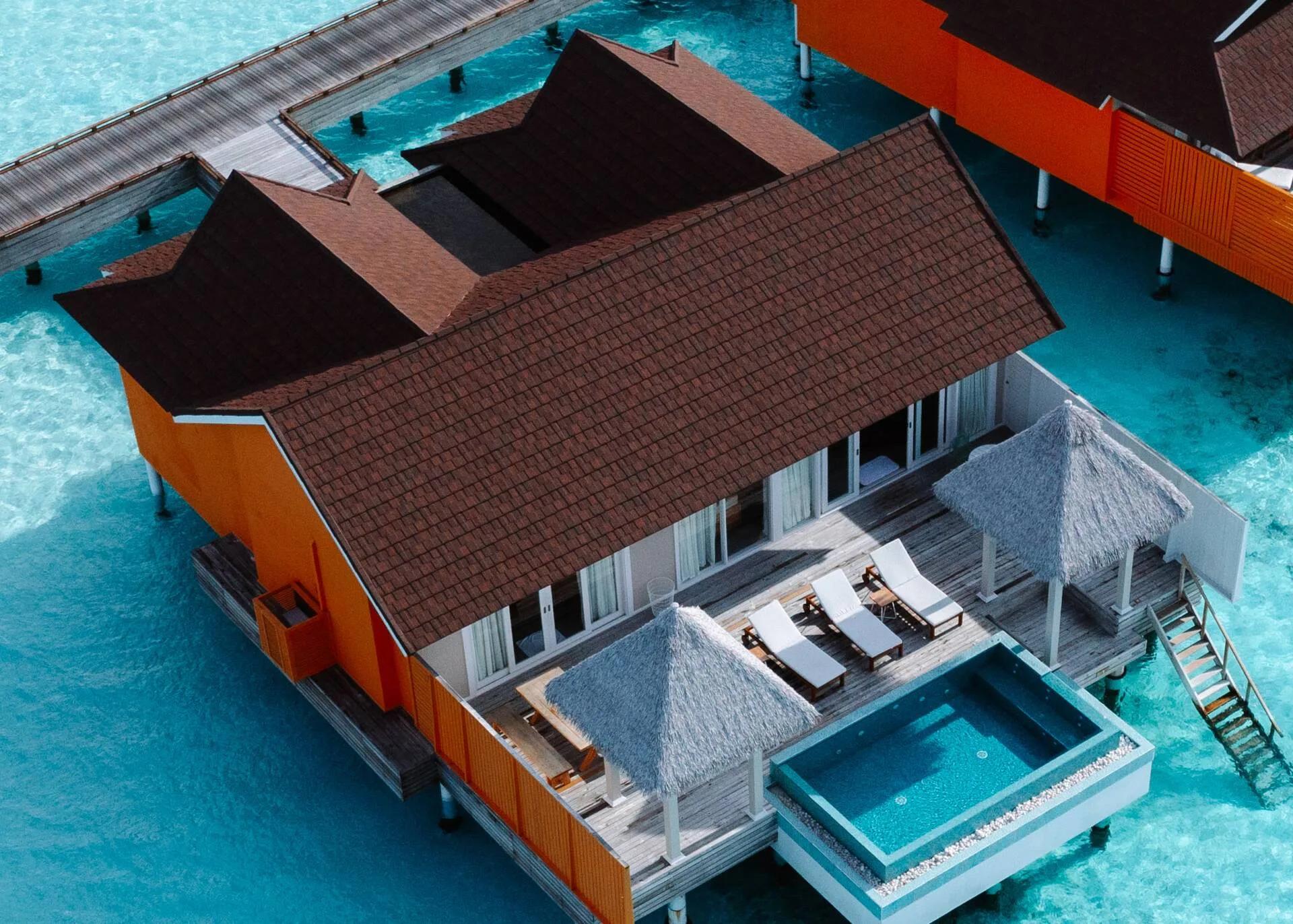 Aerial view of orange-panelled overwater villas at The Standard, private plunge pools cantilevered off each deck above the lagoon