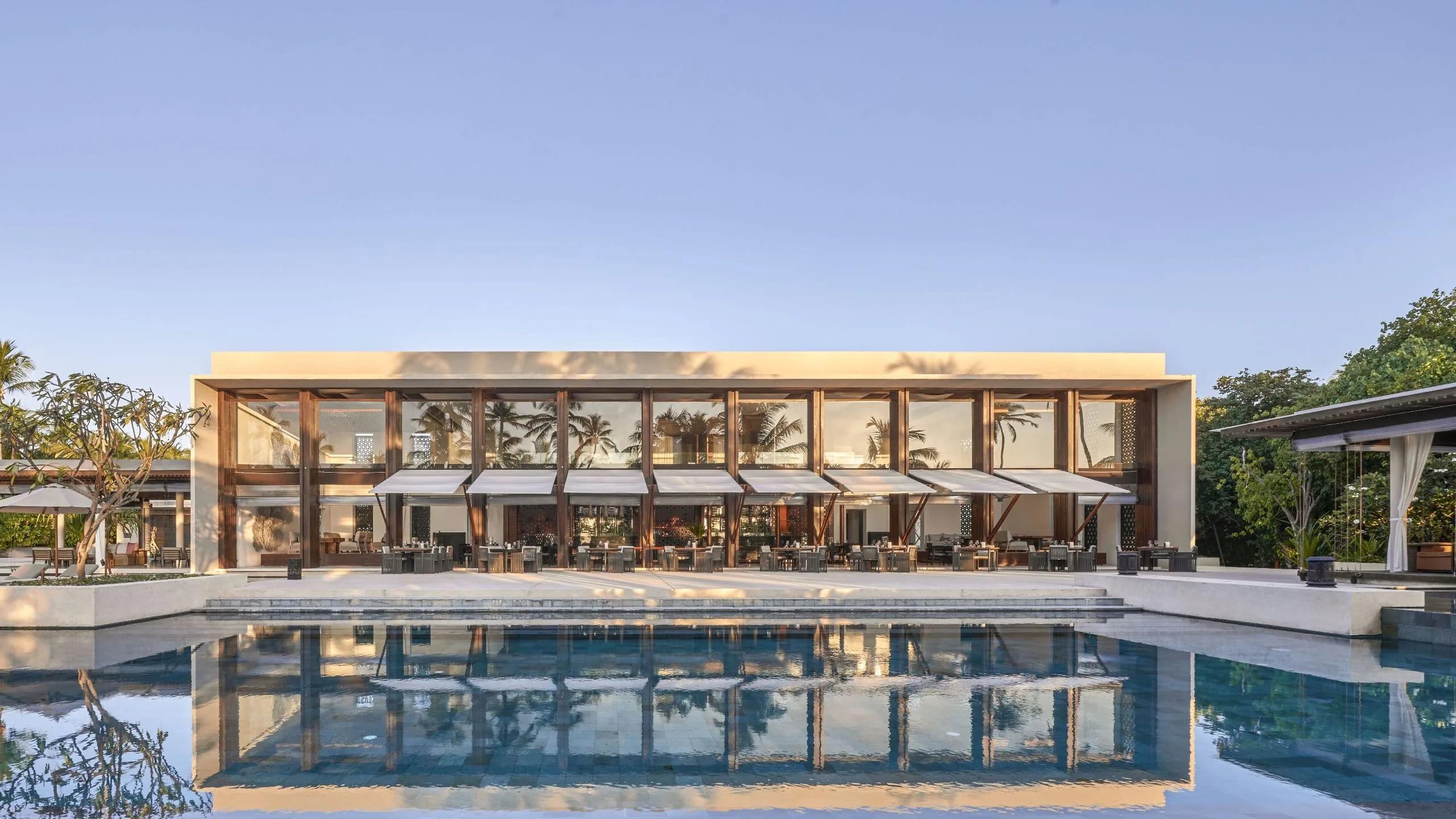 The Dining Room's glass-walled facade lit at dusk, reflected in the pool in front of it