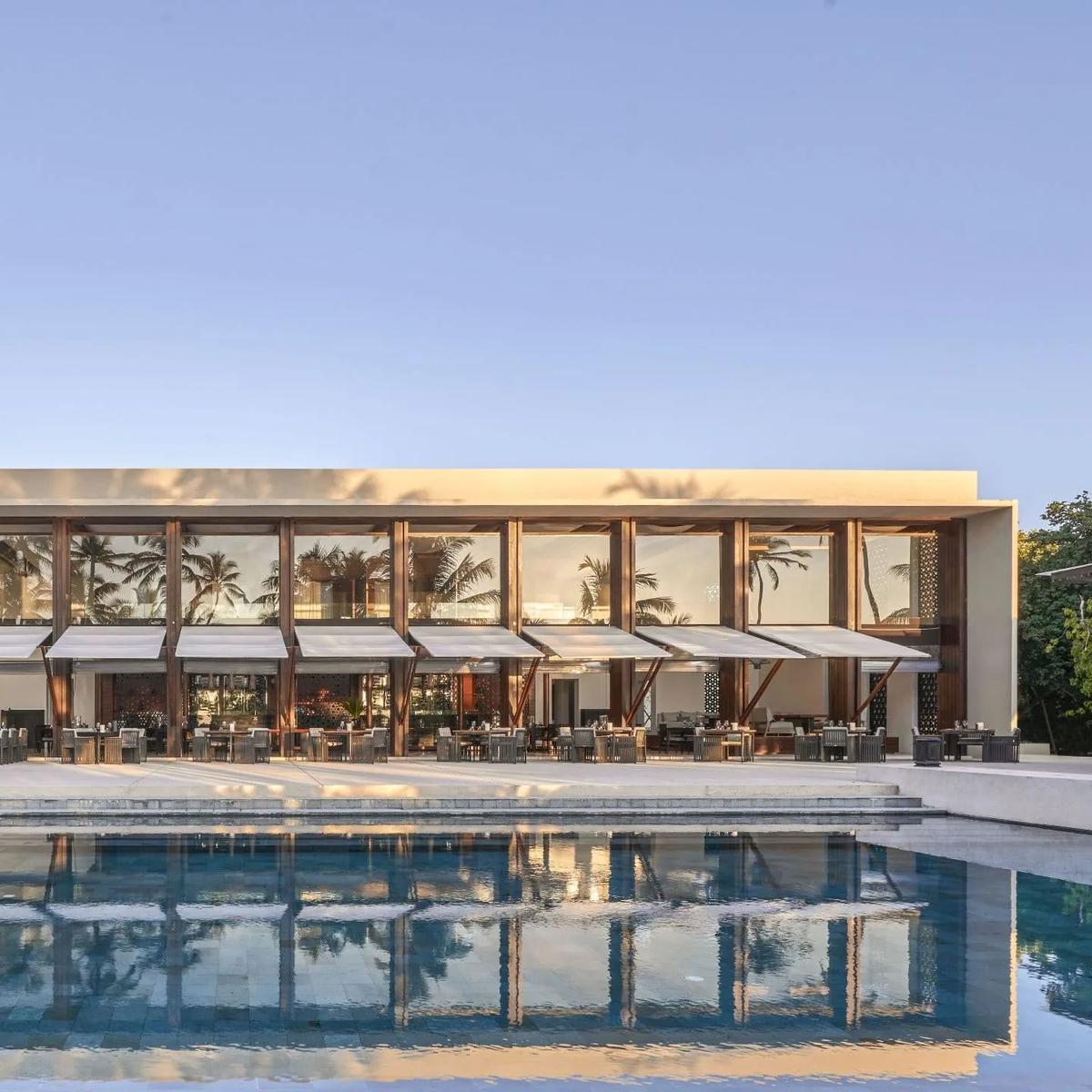 The Dining Room's glass-walled facade lit at dusk, reflected in the pool in front of it