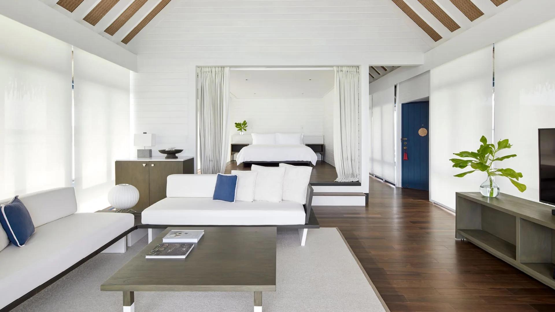 The living area of a One-Bedroom Water Villa with Pool, with a blue front door and floor-to-ceiling glass