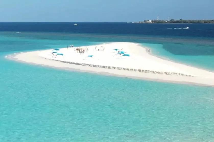 An aerial view of a sandbank picnic set up on an exposed reef flat, blue cabana tents and a small gathering of guests