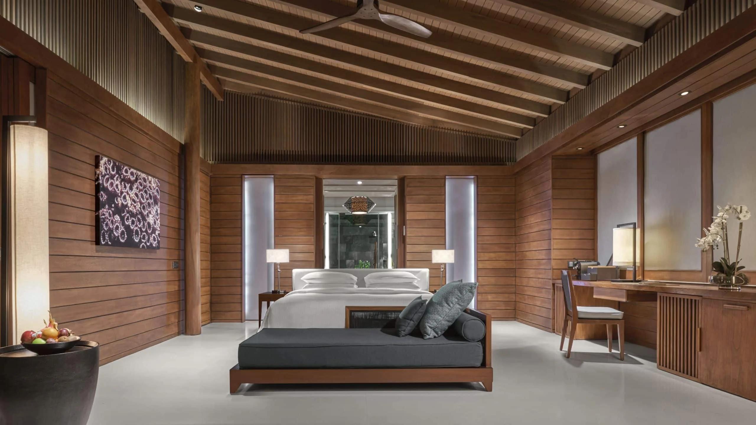 The bedroom of a Beach Villa, warm wood panelling and a daybed at the foot of the bed