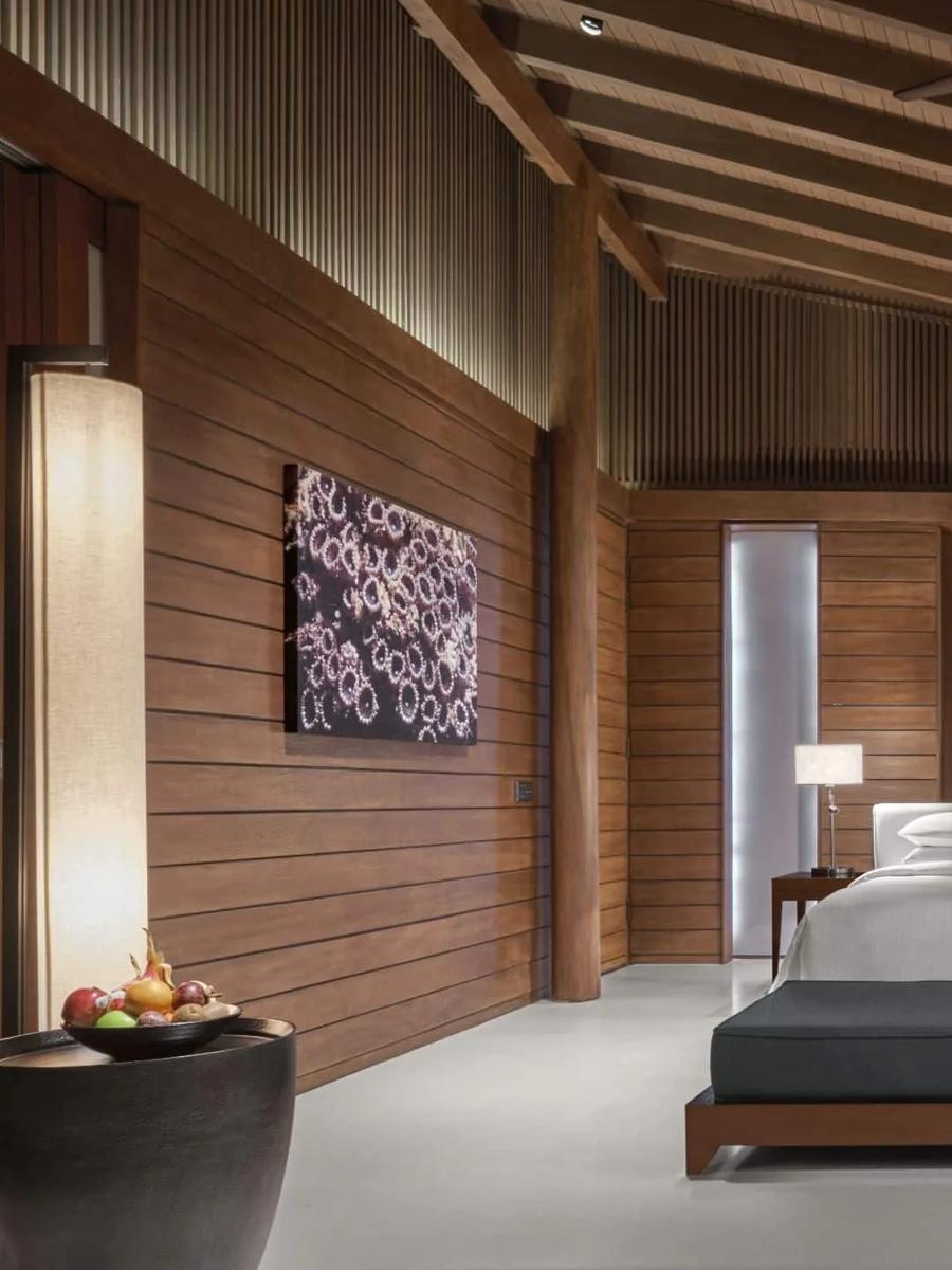 The bedroom of a Beach Villa, warm wood panelling and a daybed at the foot of the bed
