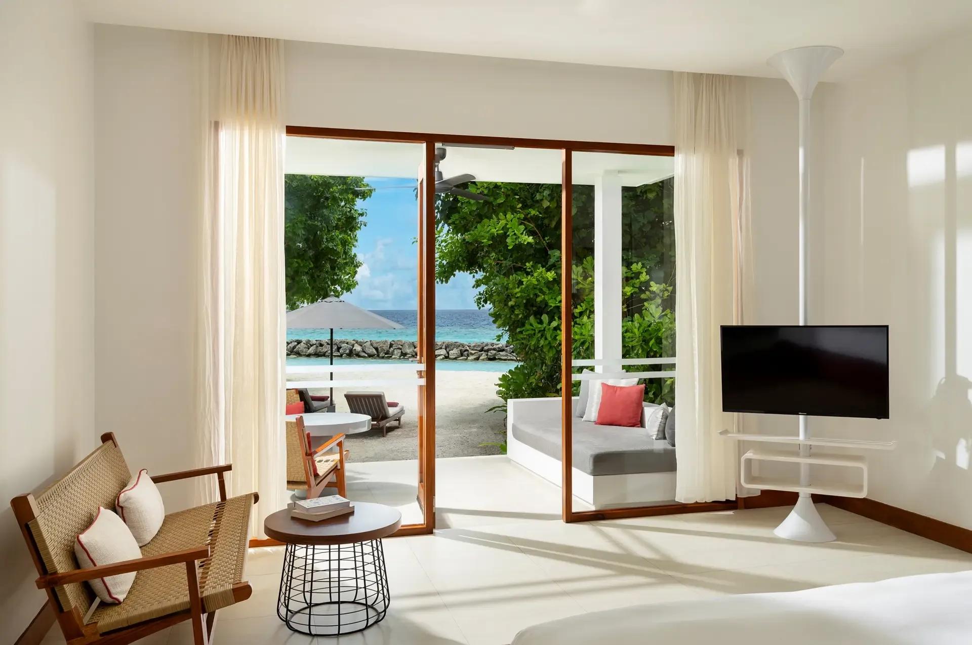 A daybed and seating area opening onto a palm-lined path to the beach from a Deluxe Beach Bungalow