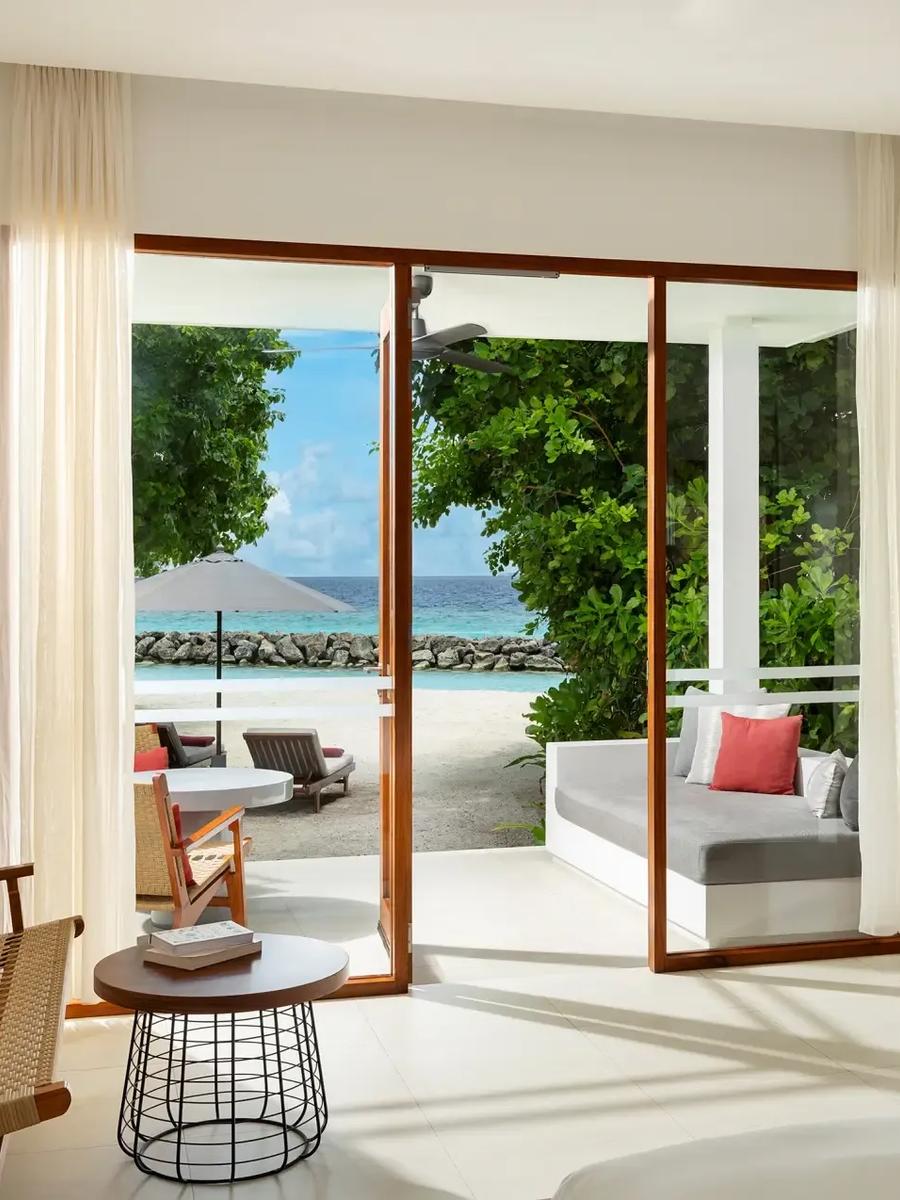 A daybed and seating area opening onto a palm-lined path to the beach from a Deluxe Beach Bungalow