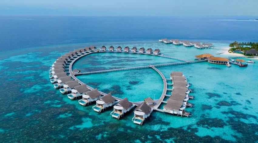 The overwater villas' horseshoe curve seen from above, jetties meeting at a central arrival pavilion