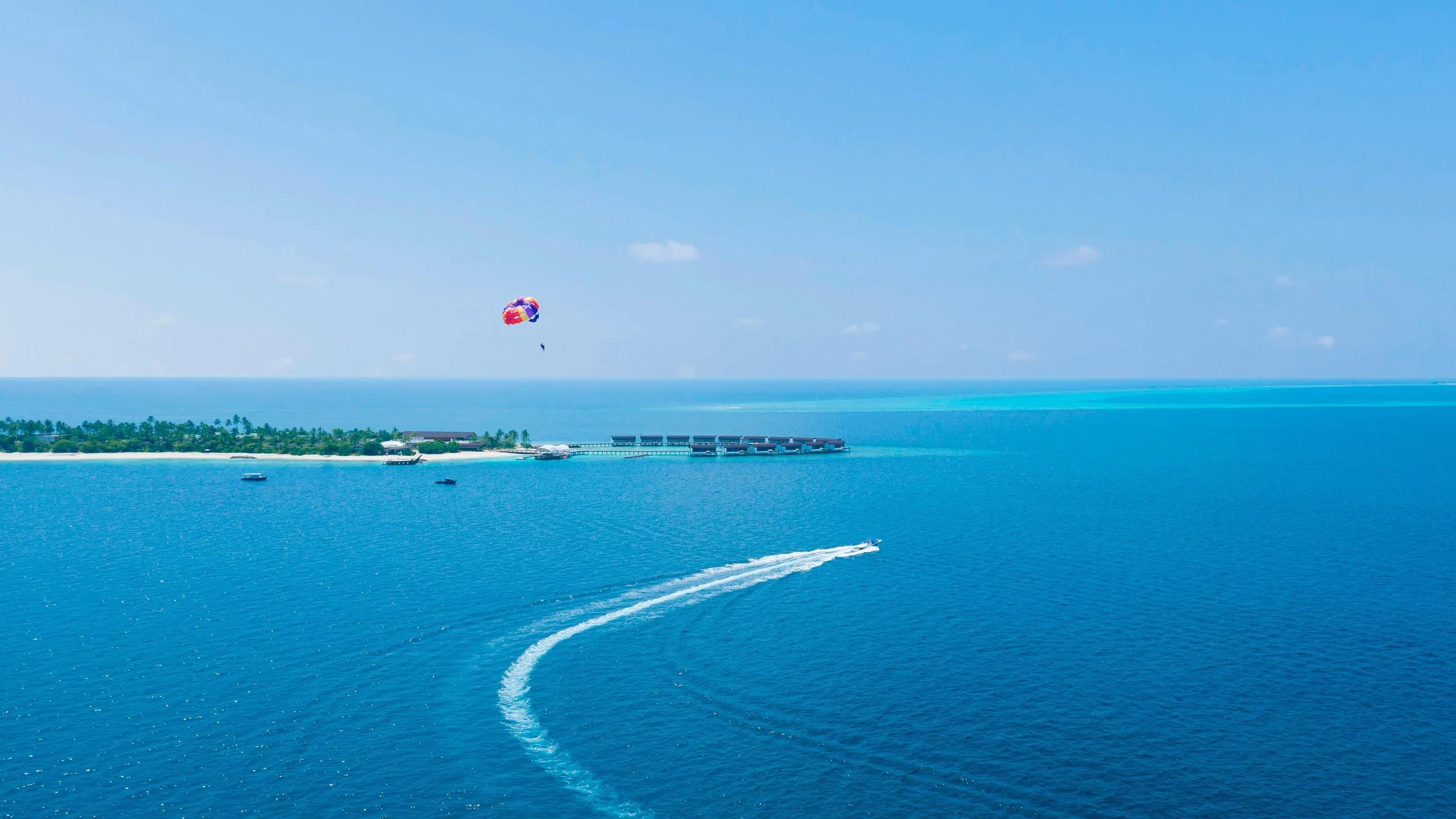 A parasailer above the lagoon with the resort's overwater villas in the distance