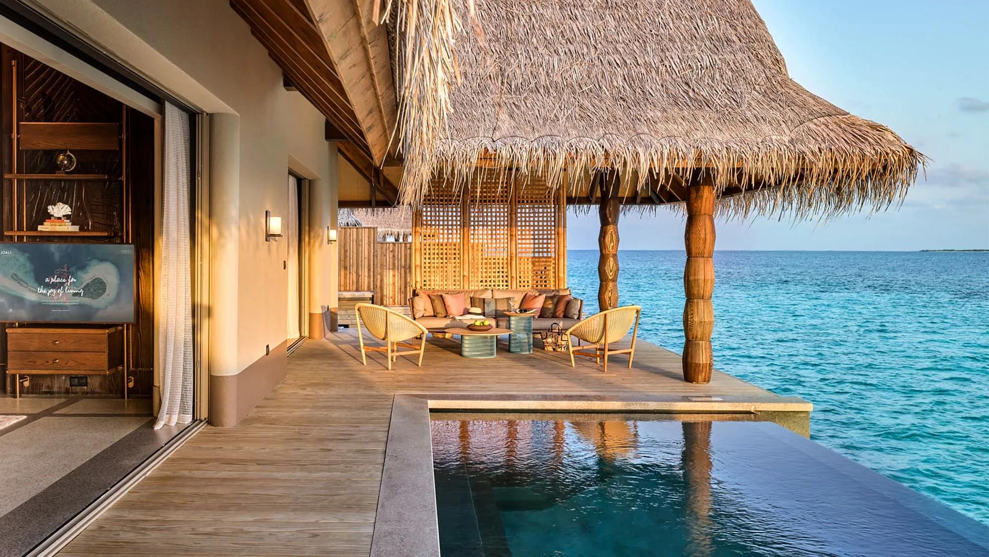 The thatched-roof deck and infinity pool of a Luxury Water Villa with Pool, daybeds and lounge chairs facing the open ocean at sunset