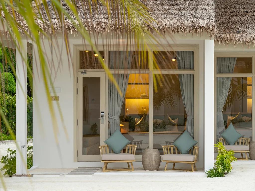The thatched-roof entrance of a Beach Villa at Bandos, with lounge chairs set on a sandy porch behind a palm frond